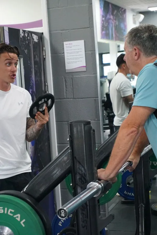 Lukas Kettle demonstrating a weight plate to an older client at a chest press machine